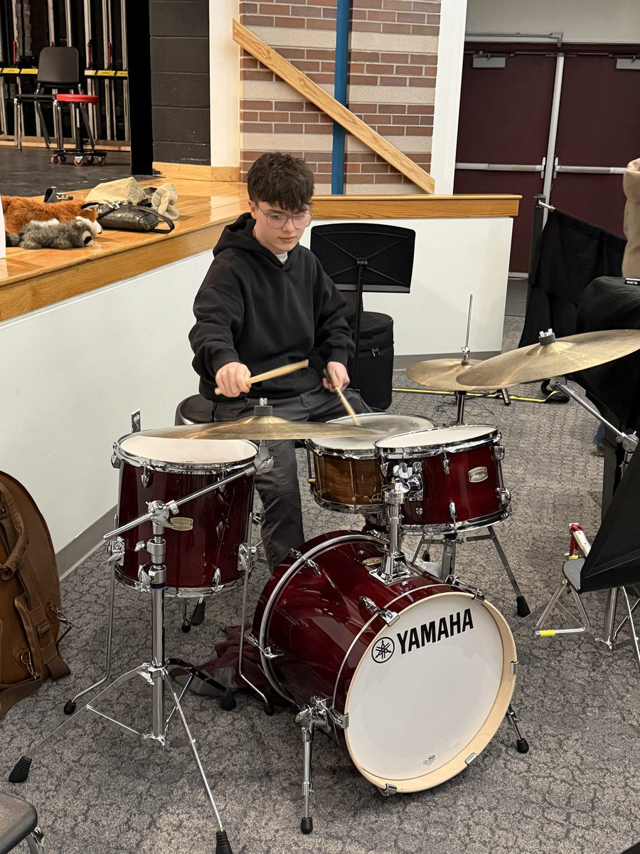 A drum student playing a red Yamaha drum kit during a lesson
